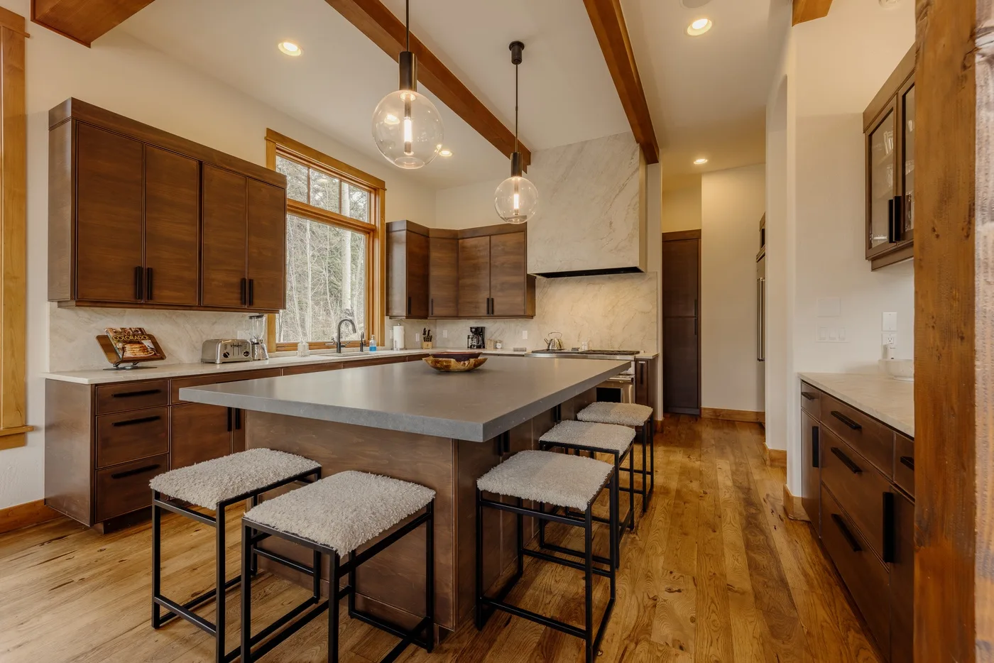 A kitchen with a large island and wooden cabinets beneath exposed ceiling beams.