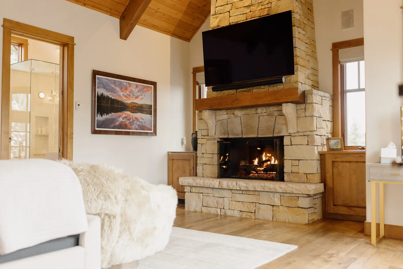 A living room with a stone fireplace and television beneath a vaulted wood ceiling.