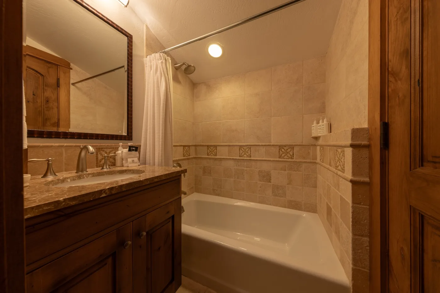 A tiled bathroom with a bathtub, shower curtain, and wooden vanity.