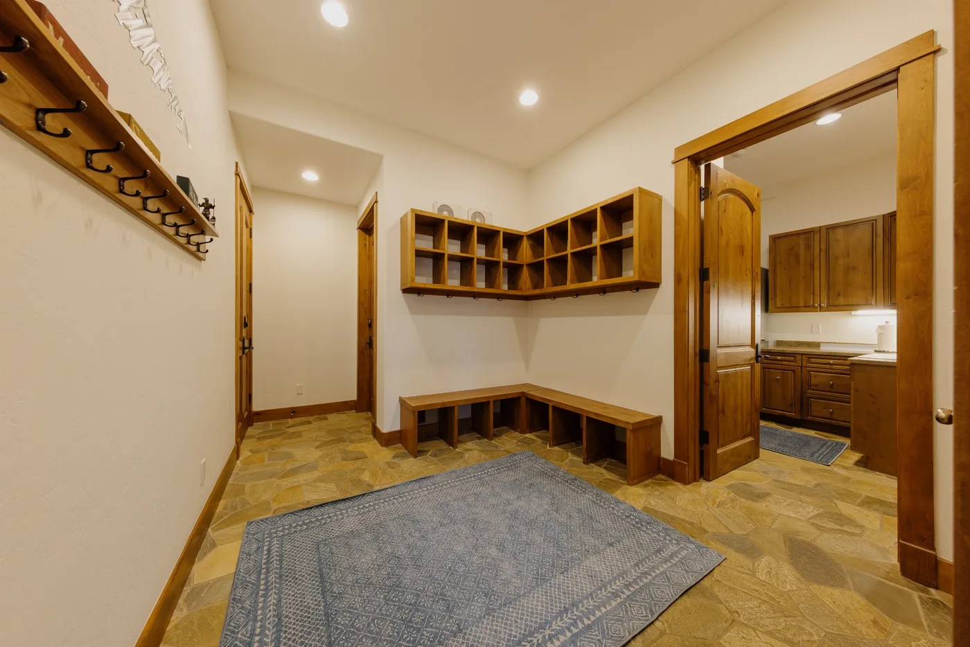 A tiled entry area has wall hooks, corner shelving, and a gray rug.