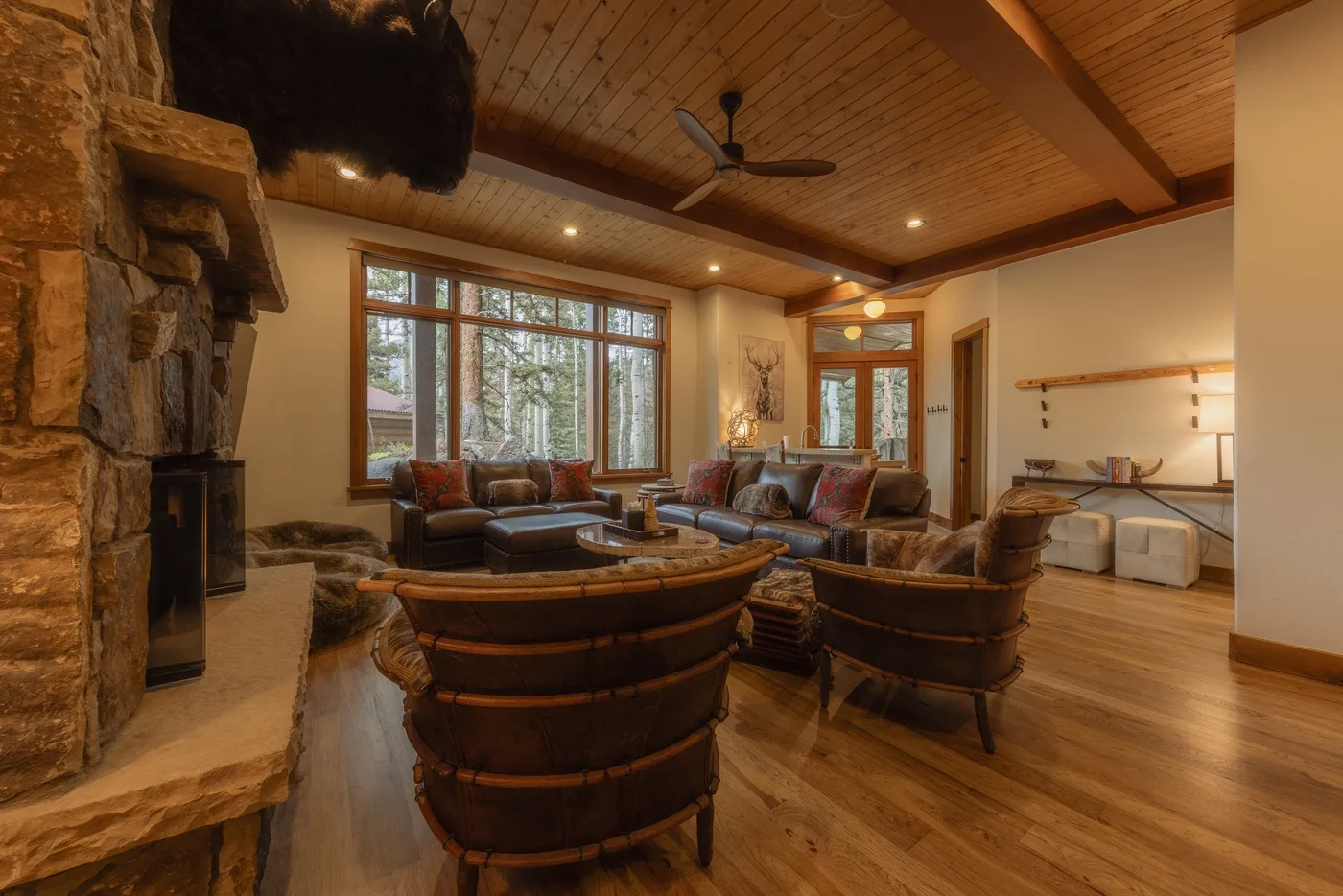 A spacious living room has comfortable seating, large windows, and a stone fireplace.