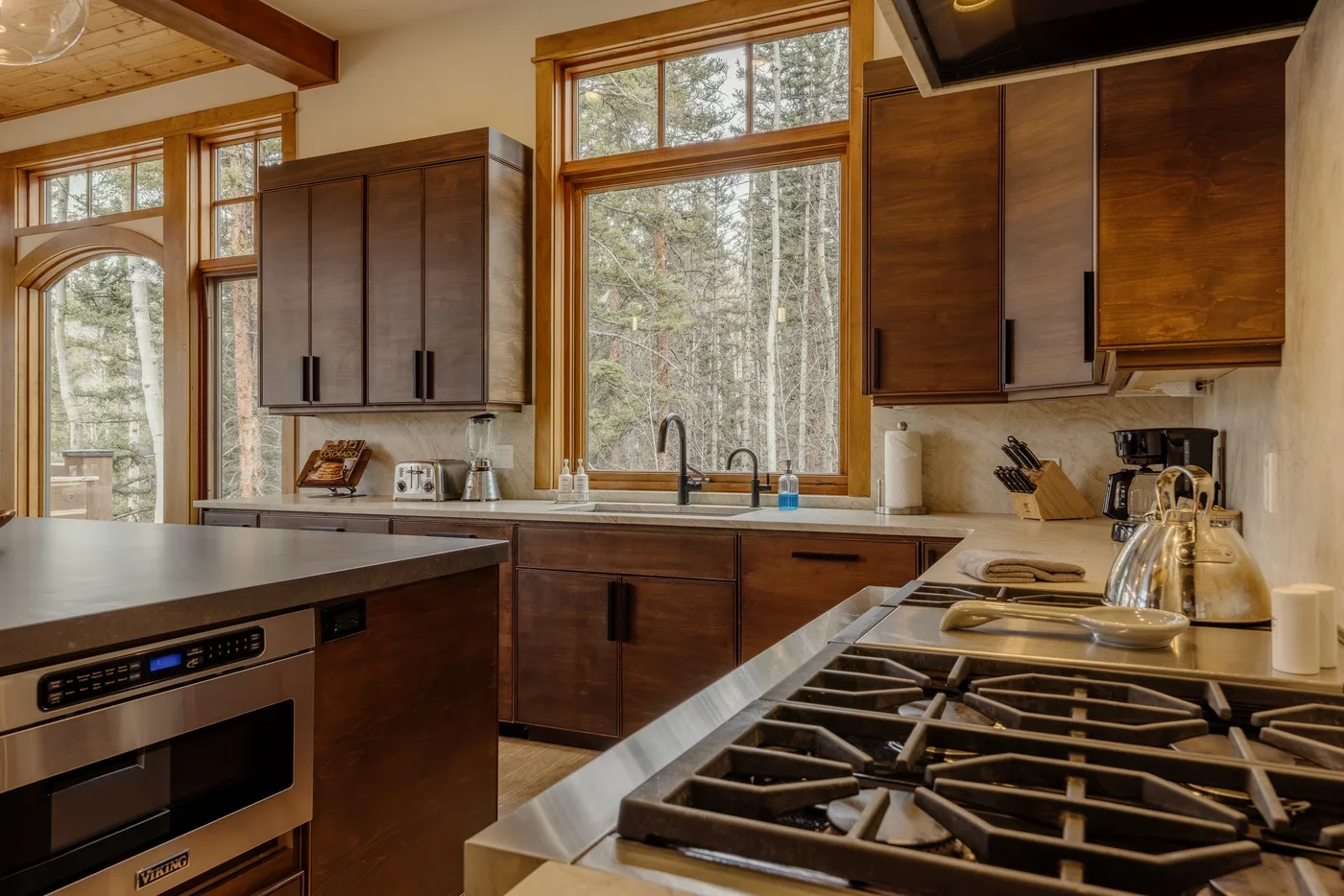 A wood-cabinet kitchen with a large central window and a gas cooktop.