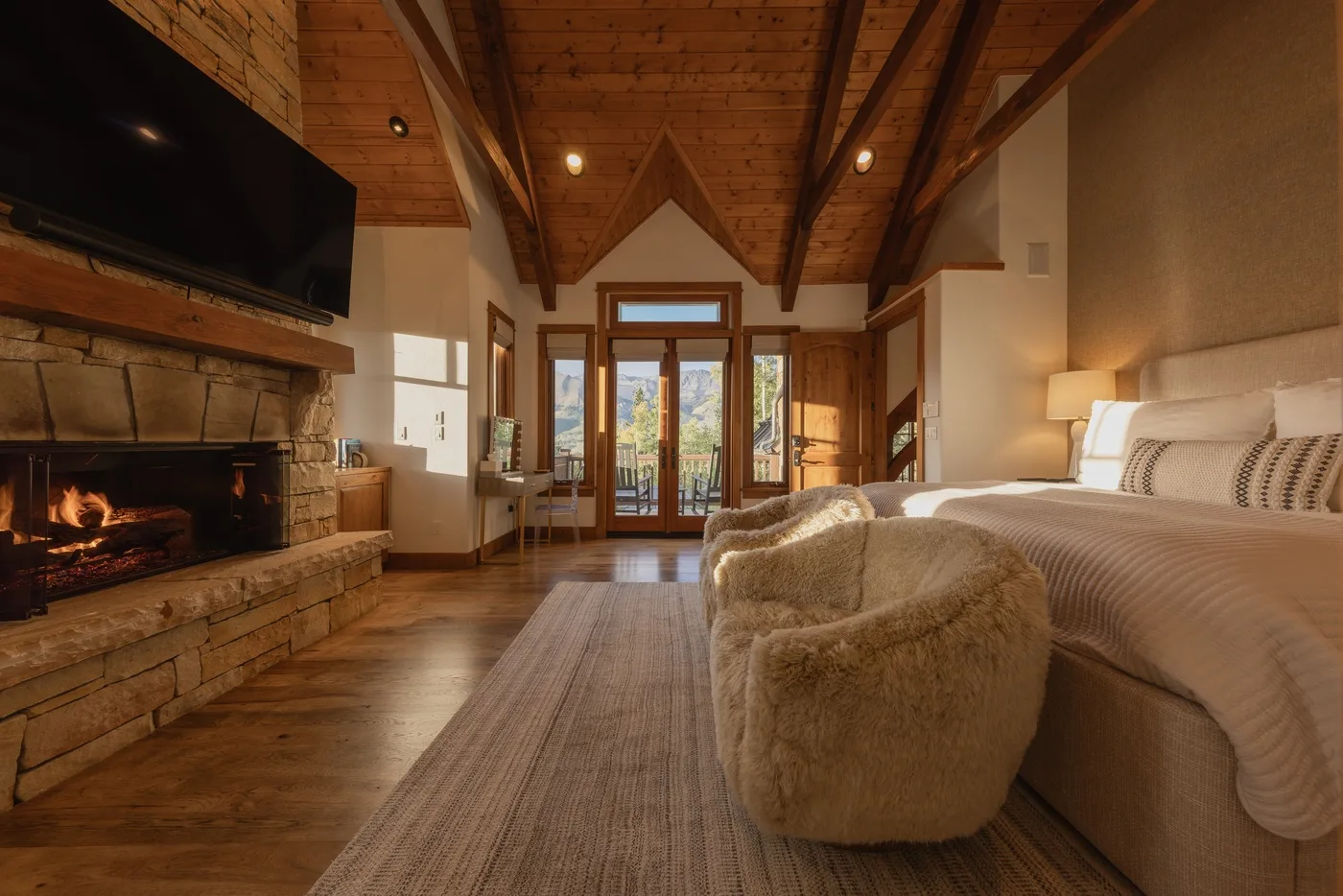A bedroom with a large bed, a fireplace, and glass doors opening onto a view.