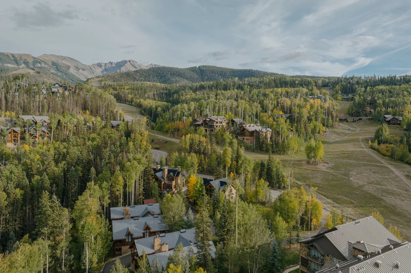 A mountain valley with scattered buildings, forested hills, and an open grassy slope.