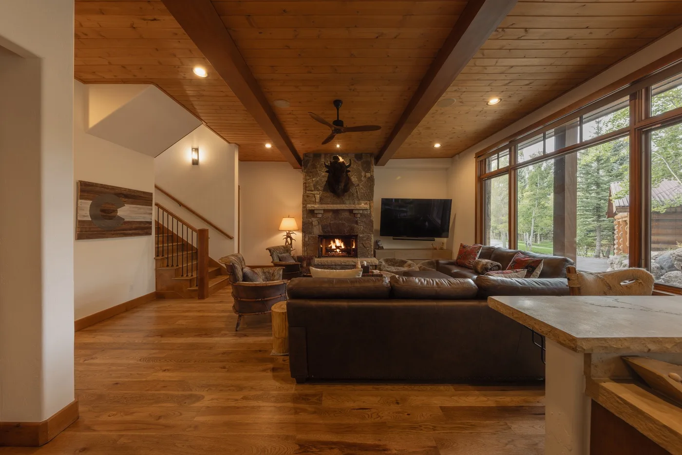 A spacious living room features wood ceilings, seating, a fireplace, and large windows.