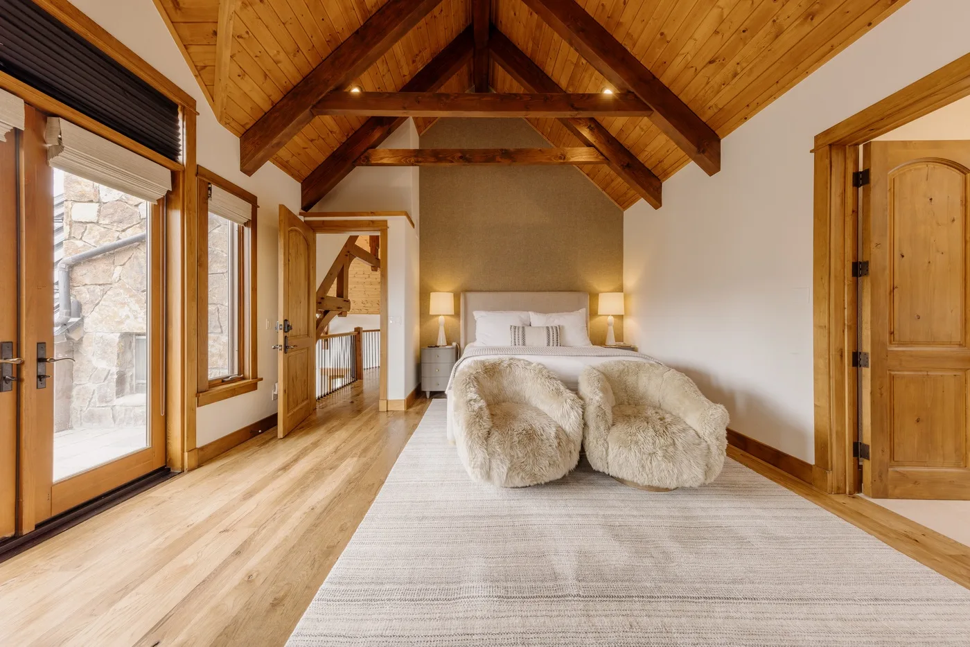 A bedroom with a bed, bedside lamps, and a vaulted wooden ceiling.