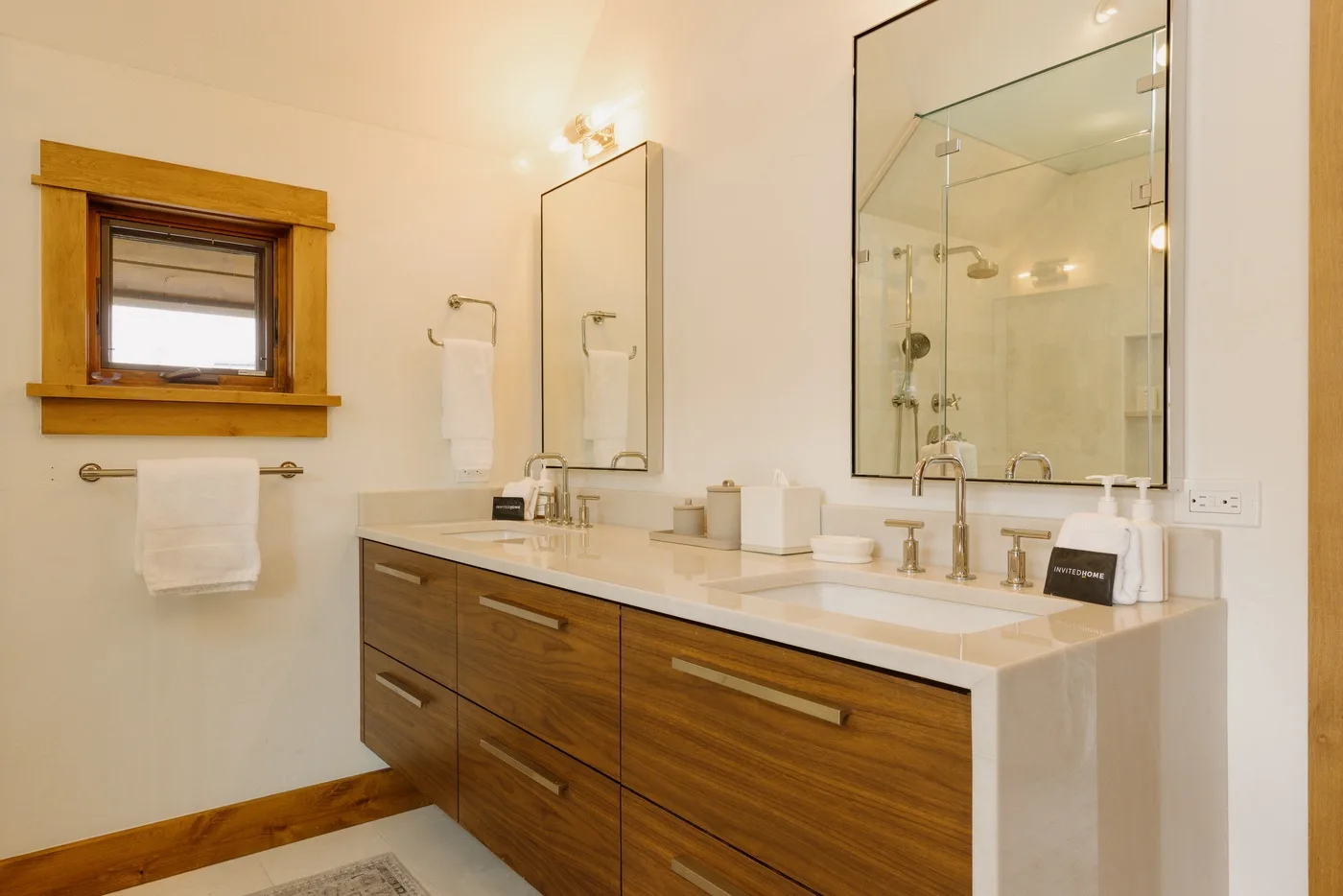 A bright bathroom with a double-sink vanity, large mirror, and glass shower.