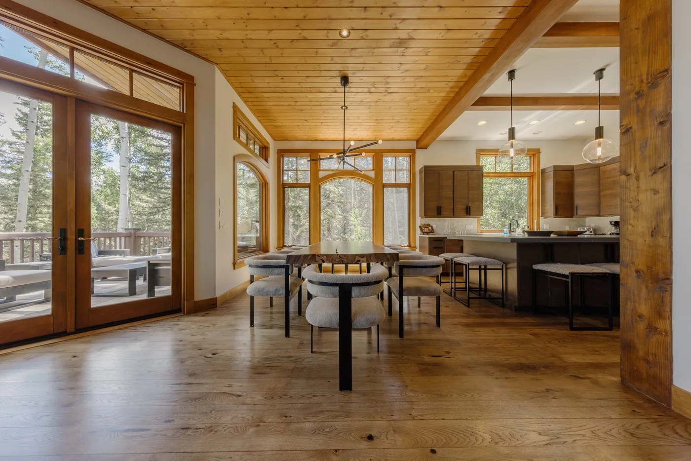 A dining area with a long table and chairs opens onto a kitchen.