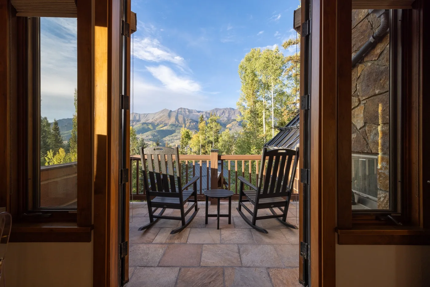 A patio with rocking chairs and a table overlooks a mountain landscape.
