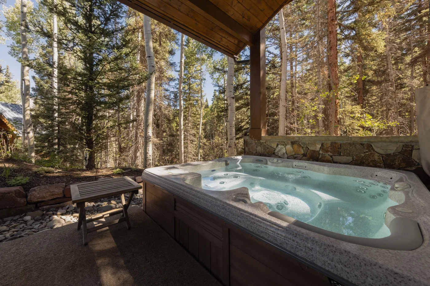 An outdoor hot tub sits beneath a wooden canopy, surrounded by trees.