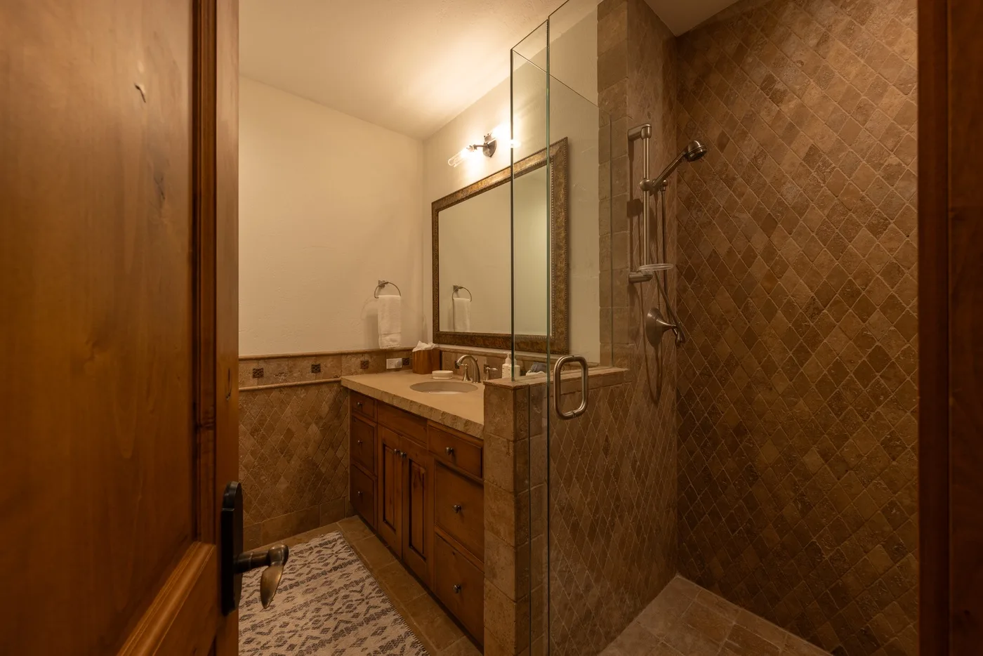 A bathroom vanity with a mirror sits beside a tiled shower.