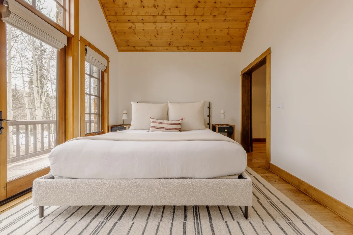 A bedroom with a large bed, windows, and a wood-paneled ceiling.