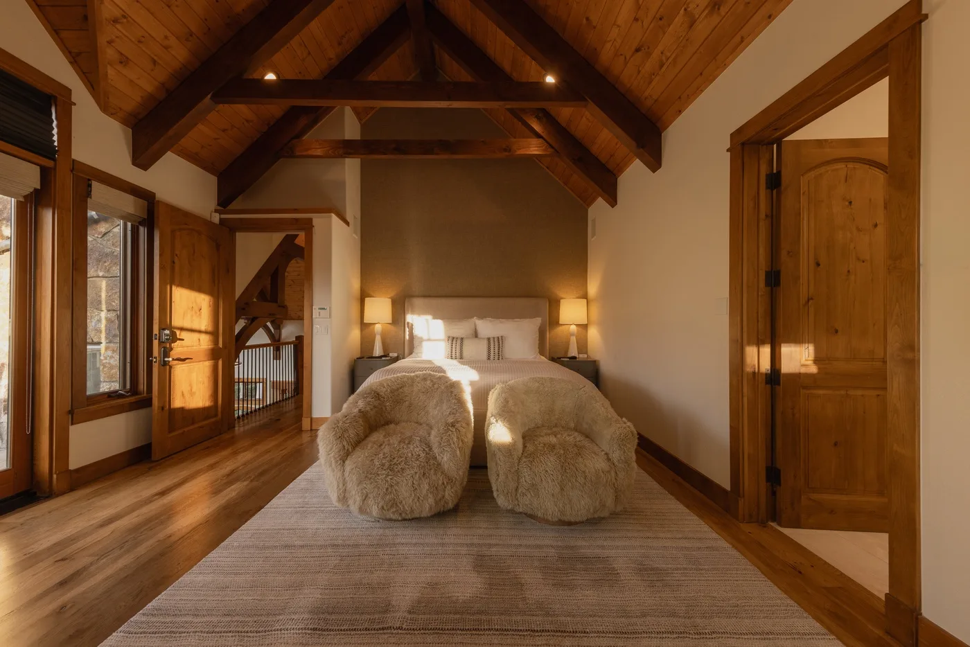 A warmly lit bedroom with a bed beneath a high exposed-beam wooden ceiling.