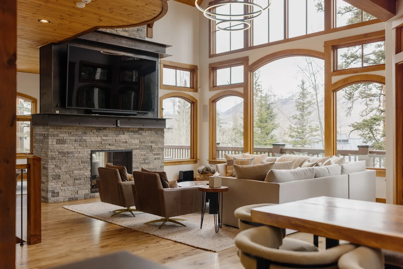 A spacious living room with a stone fireplace, seating, and large windows.