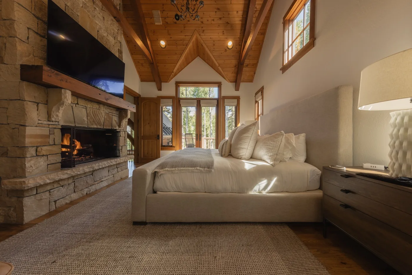 A bedroom with a bed facing a stone fireplace and television.