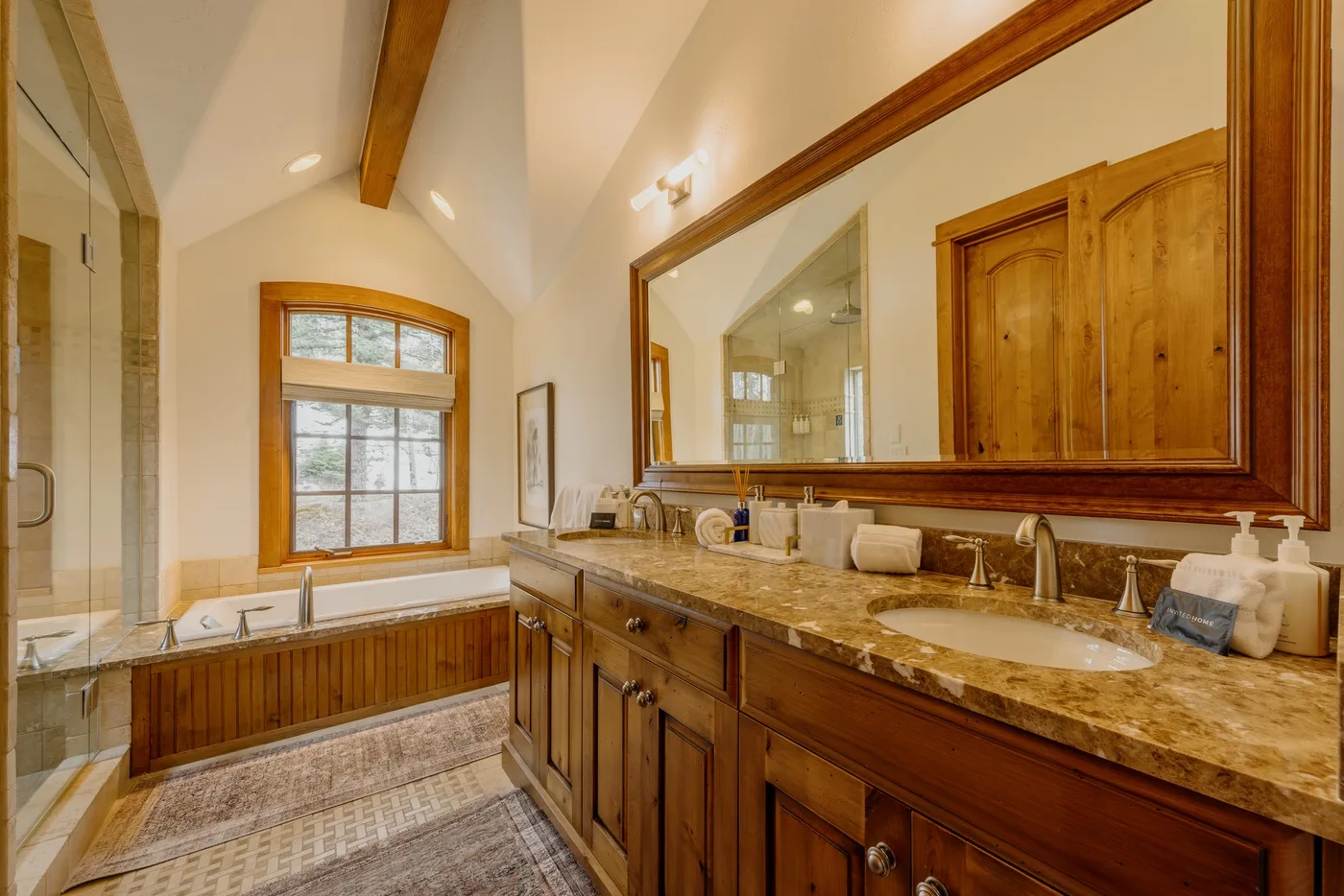A bright bathroom with a long wooden vanity, mirror, and soaking tub.