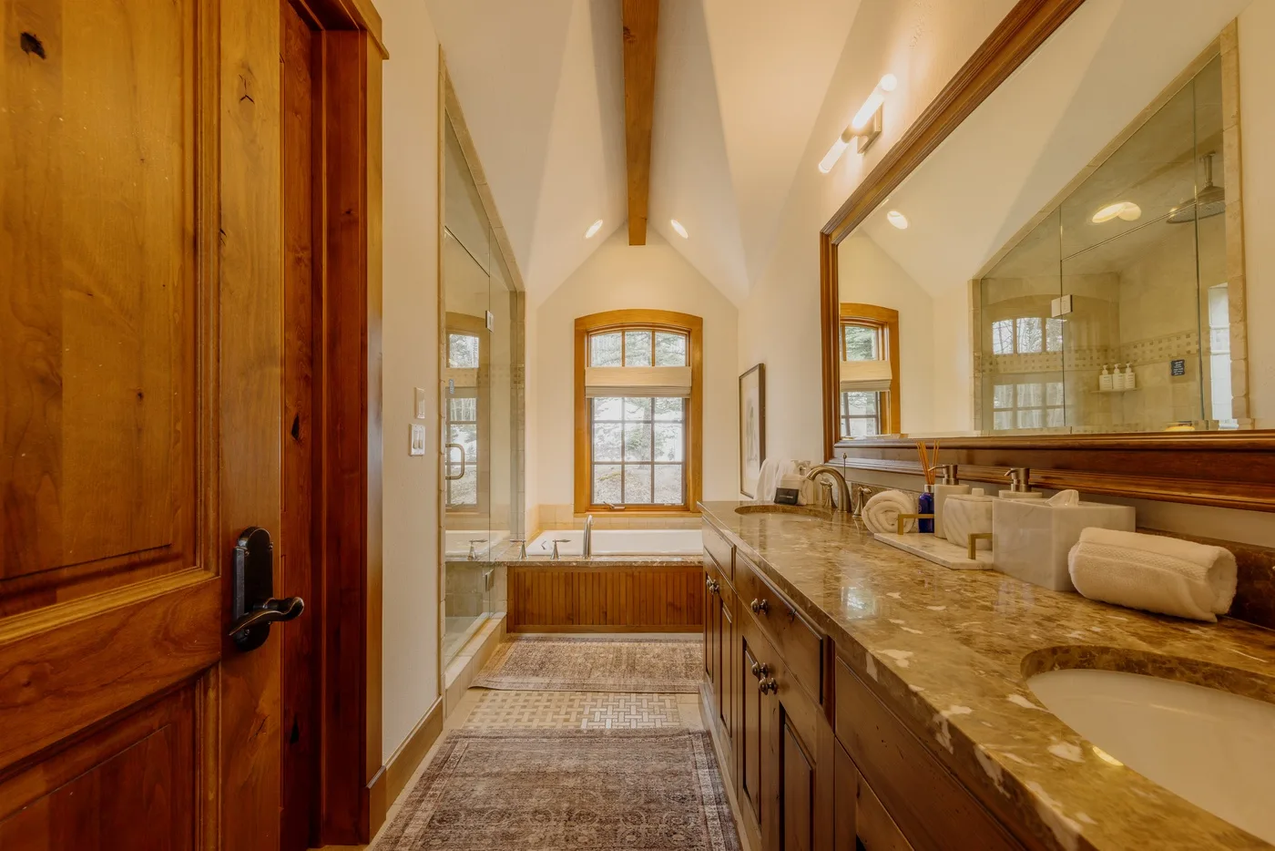 A long bathroom vanity faces a glass shower beneath a vaulted ceiling.