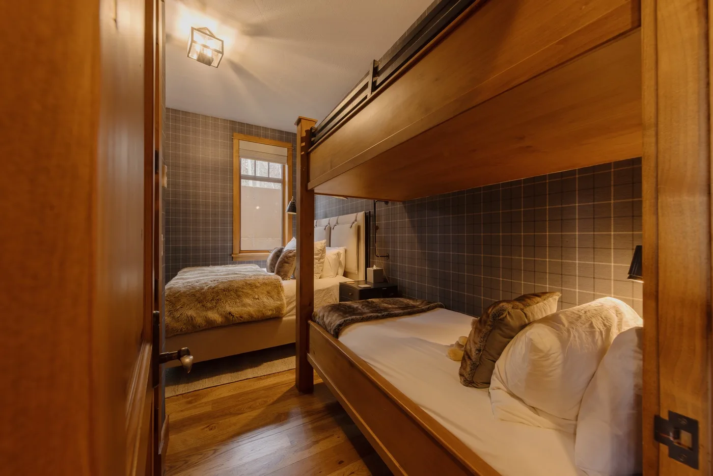 A bedroom with wooden bunk beds, patterned wall tiles, and a window.