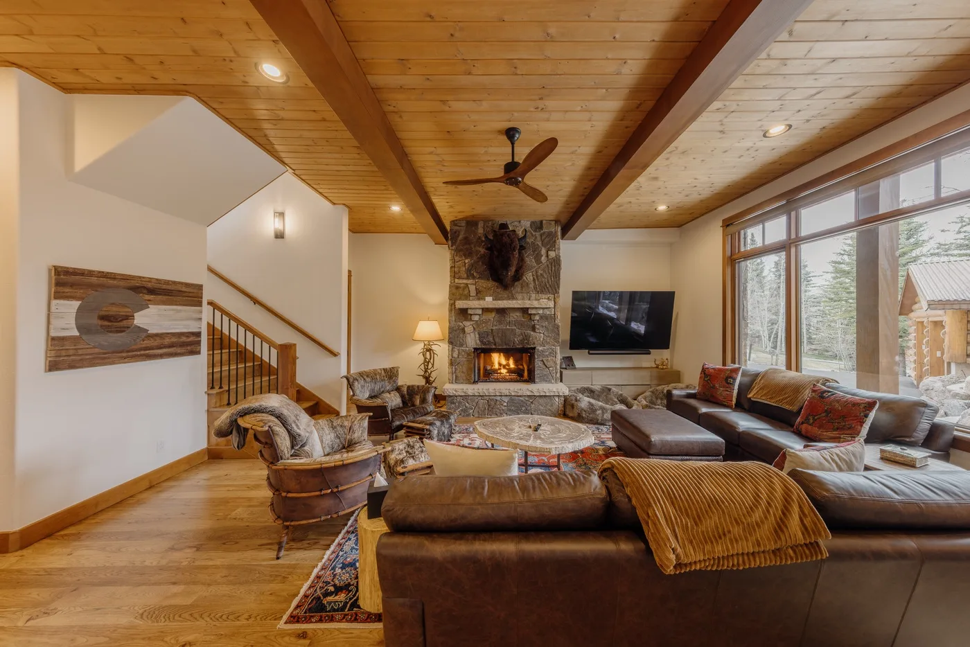 A spacious living room with a stone fireplace and seating beneath a wood-paneled ceiling.
