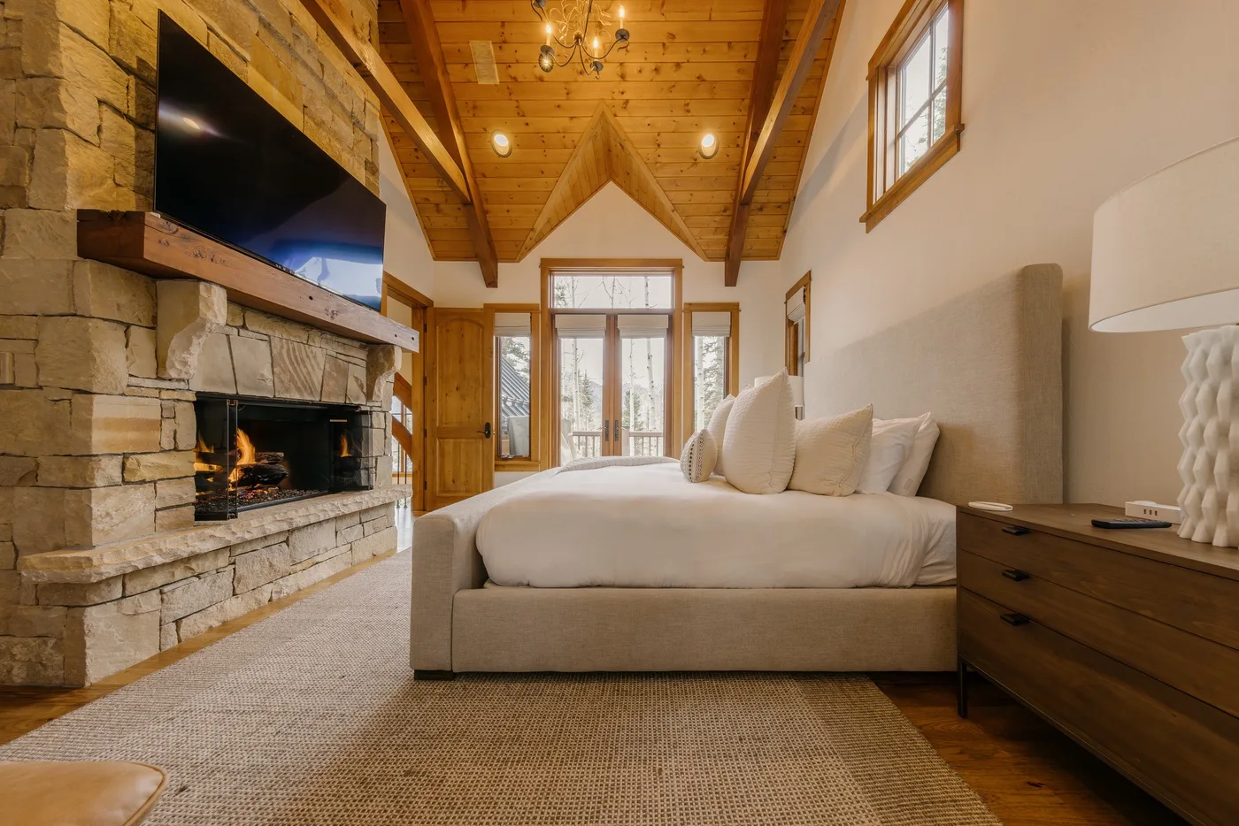A bedroom with a large bed, stone fireplace, and exposed wooden ceiling beams.