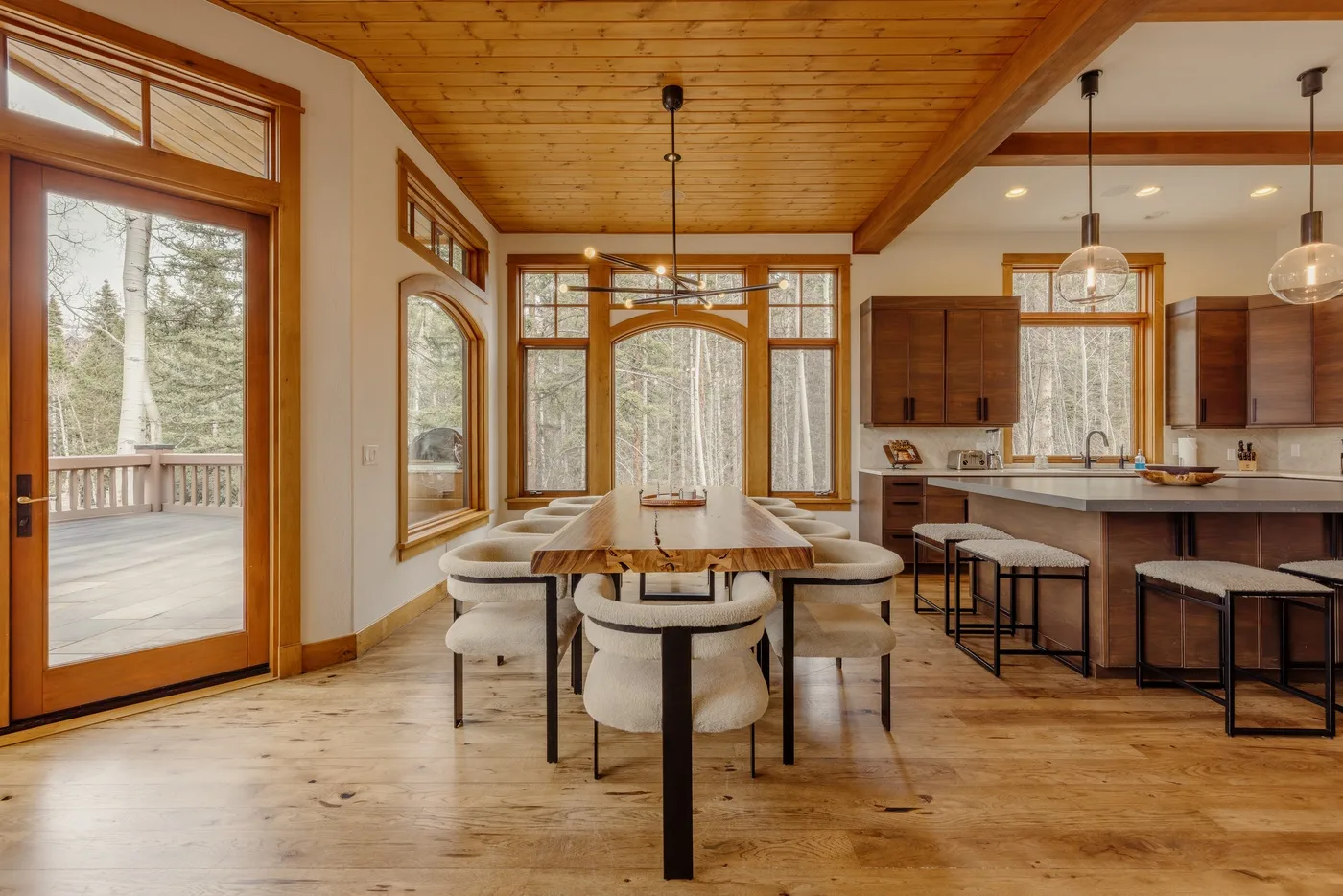 A dining area with a long table sits beside an open kitchen with a counter.