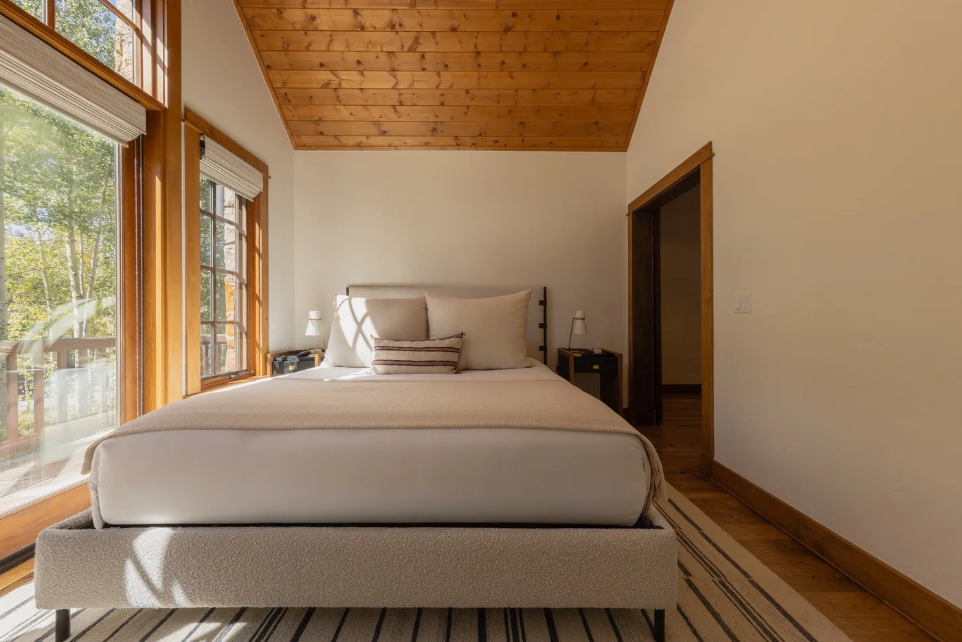 A bedroom with a neatly made bed beneath a wooden ceiling.