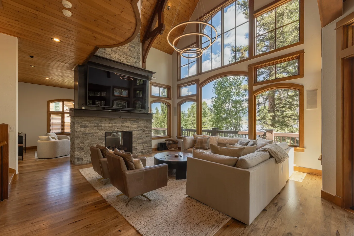 A spacious living room with seating arranged around a stone fireplace and large windows.