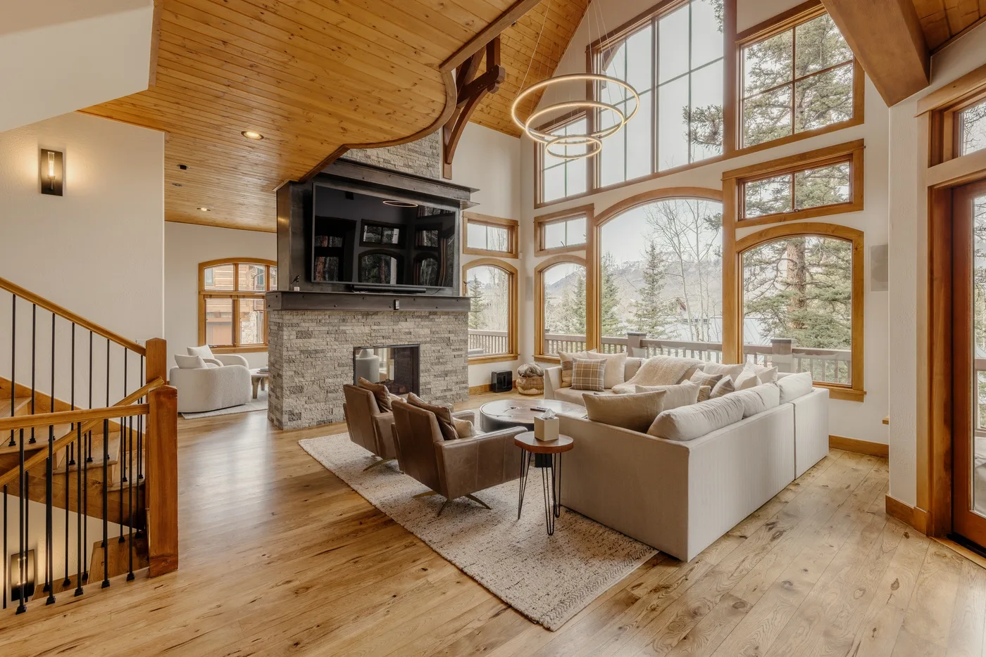 A spacious living room features seating around a stone fireplace and large windows.