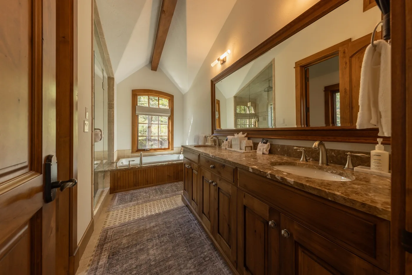 A bathroom with a long vanity, large mirror, and a soaking tub beneath the window.