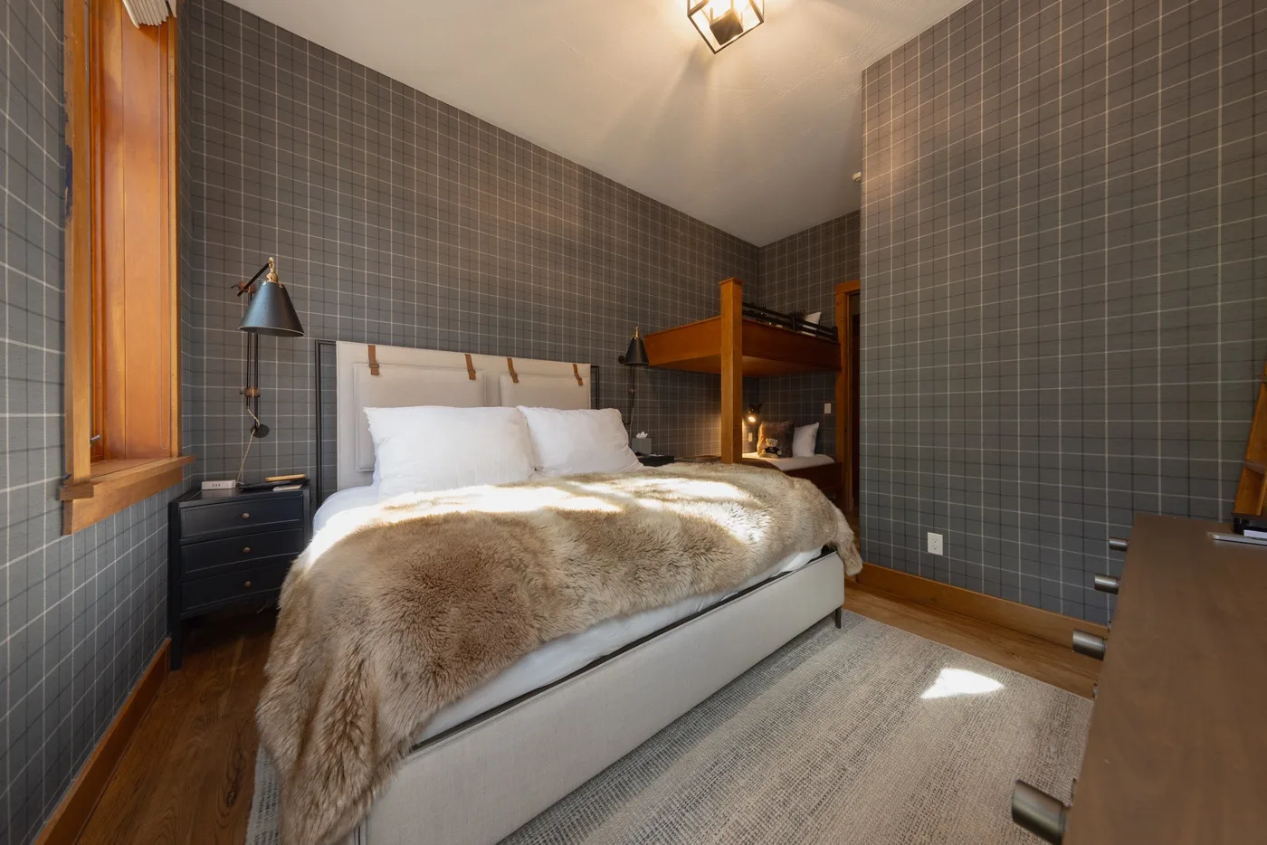A bedroom with a bed, a bunk above it, and dark tiled walls.
