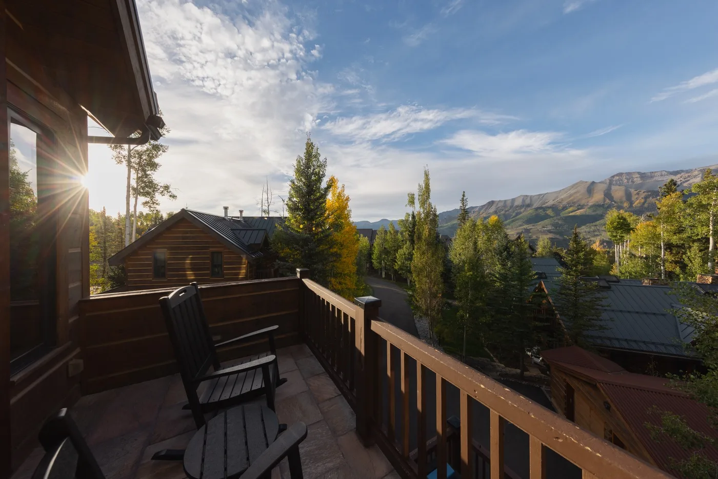A wooden balcony overlooks nearby rooftops, trees, and distant mountains.