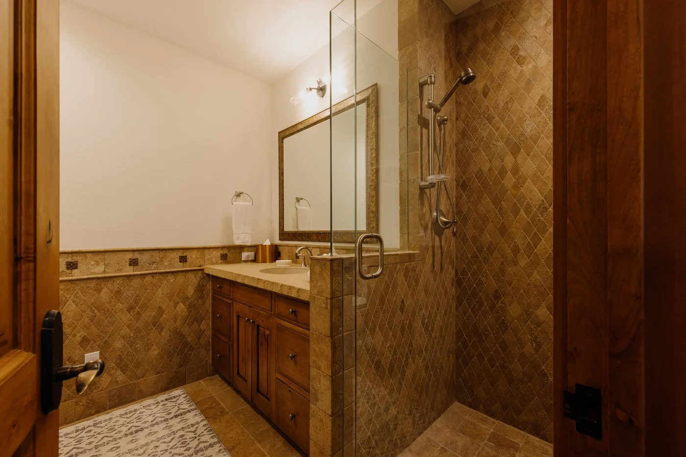 A warm-toned bathroom with a vanity, mirror, and glass shower.