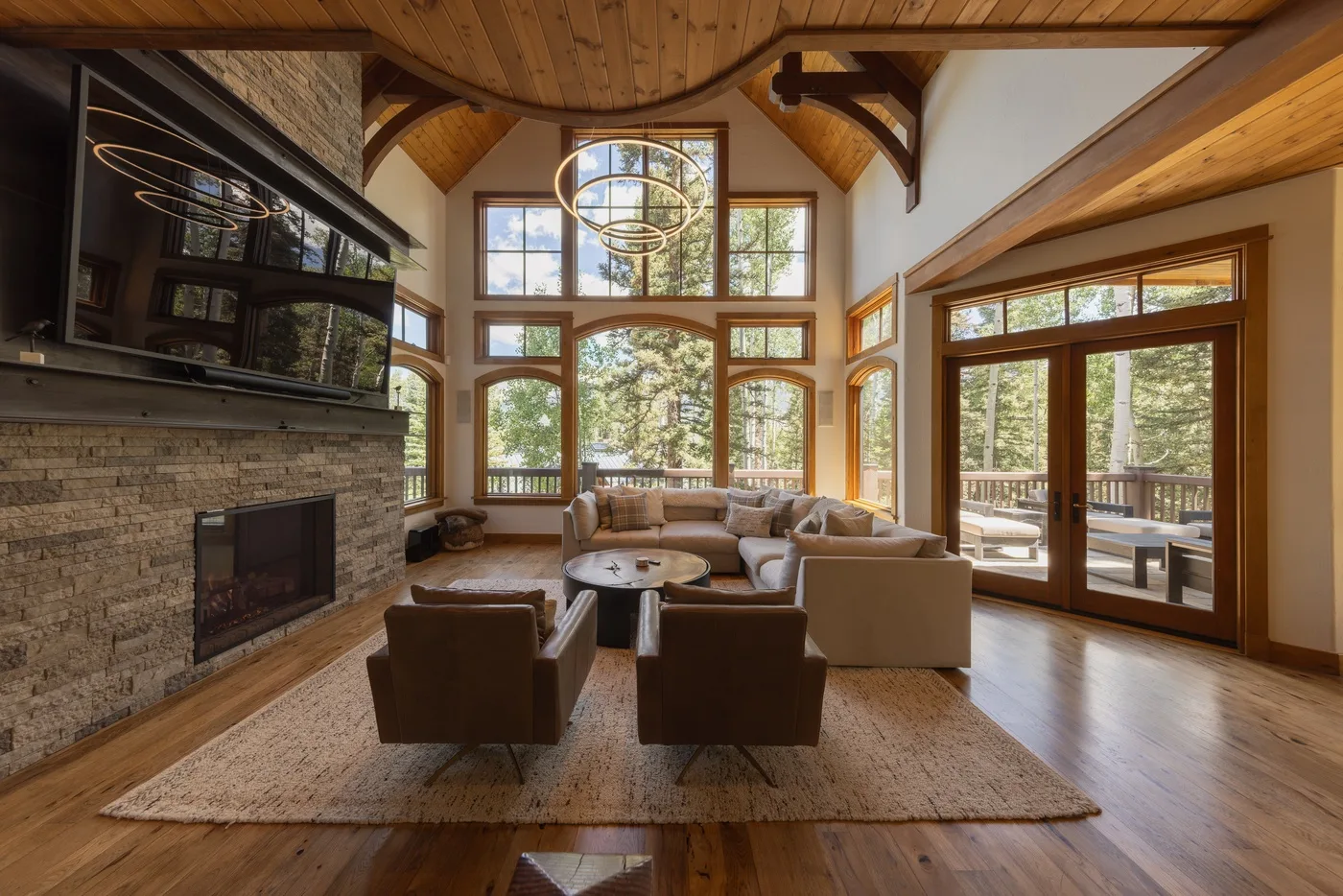 A spacious living room with seating arranged around a stone fireplace and large windows.