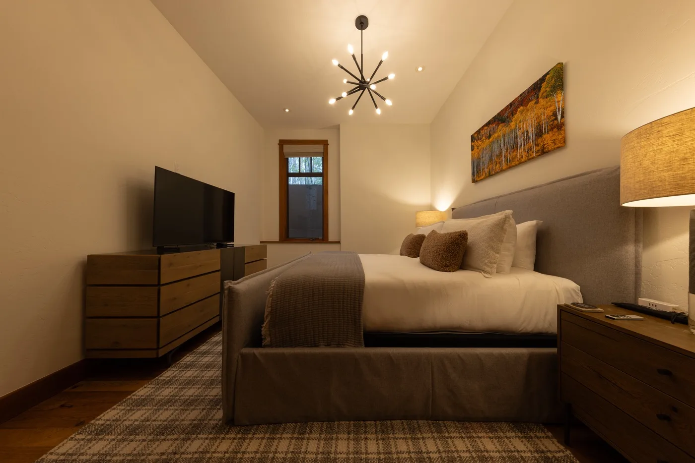 A warmly lit bedroom with a bed, television, and bedside tables.