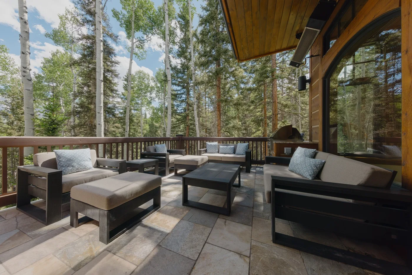 An outdoor patio seating area with cushioned furniture and a forest view.