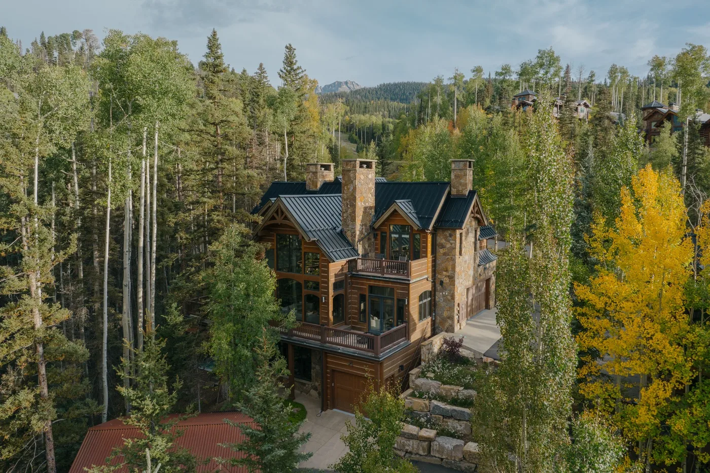 A multi-level lodge sits among dense trees, with a stone path beside it.