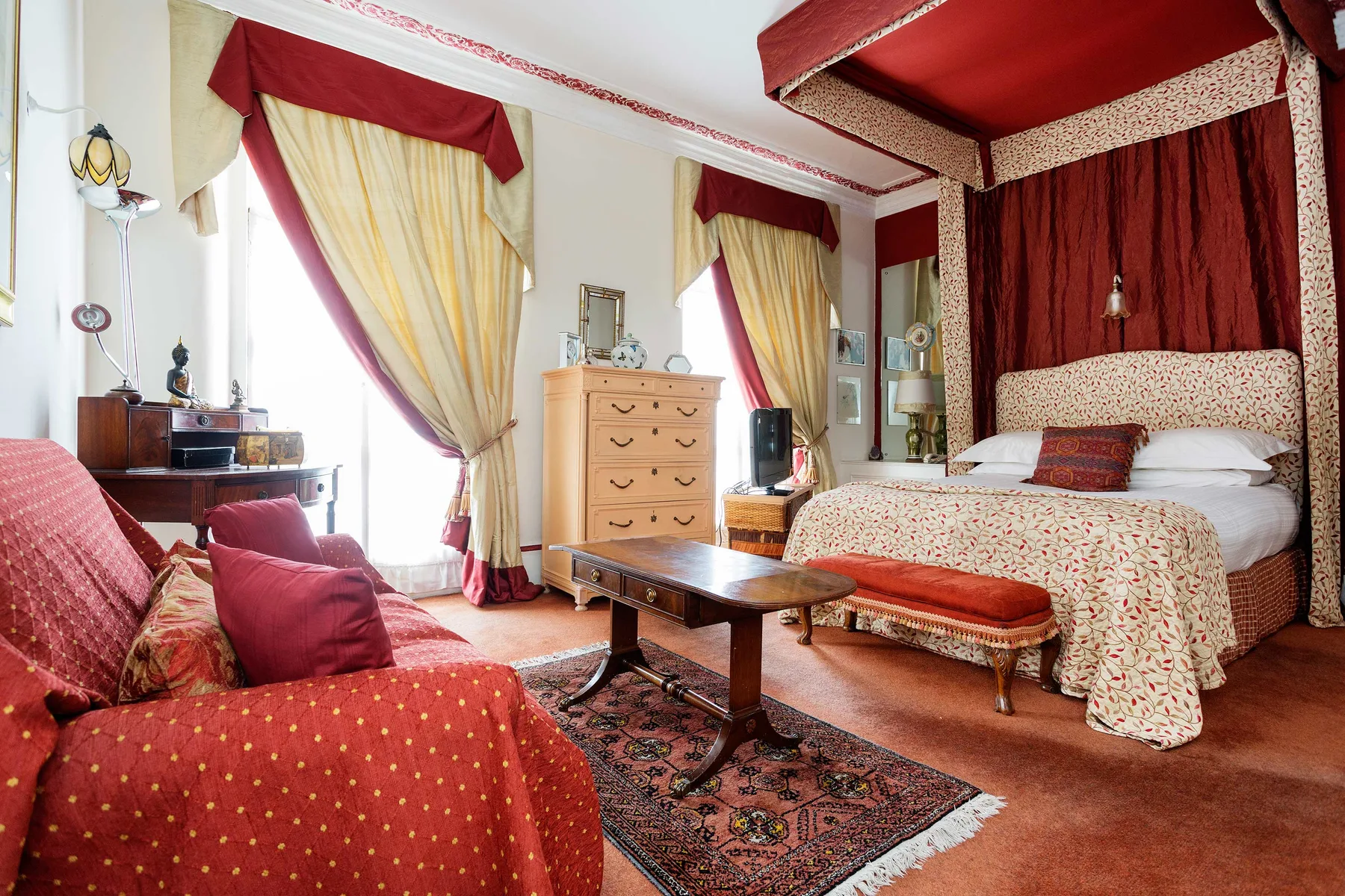 A bedroom with a large bed, patterned curtains, and a seating area.