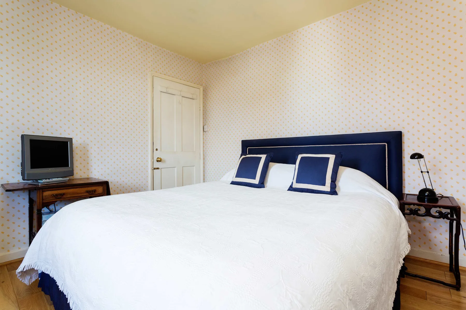 A bedroom with a large bed, patterned wallpaper, and a television.