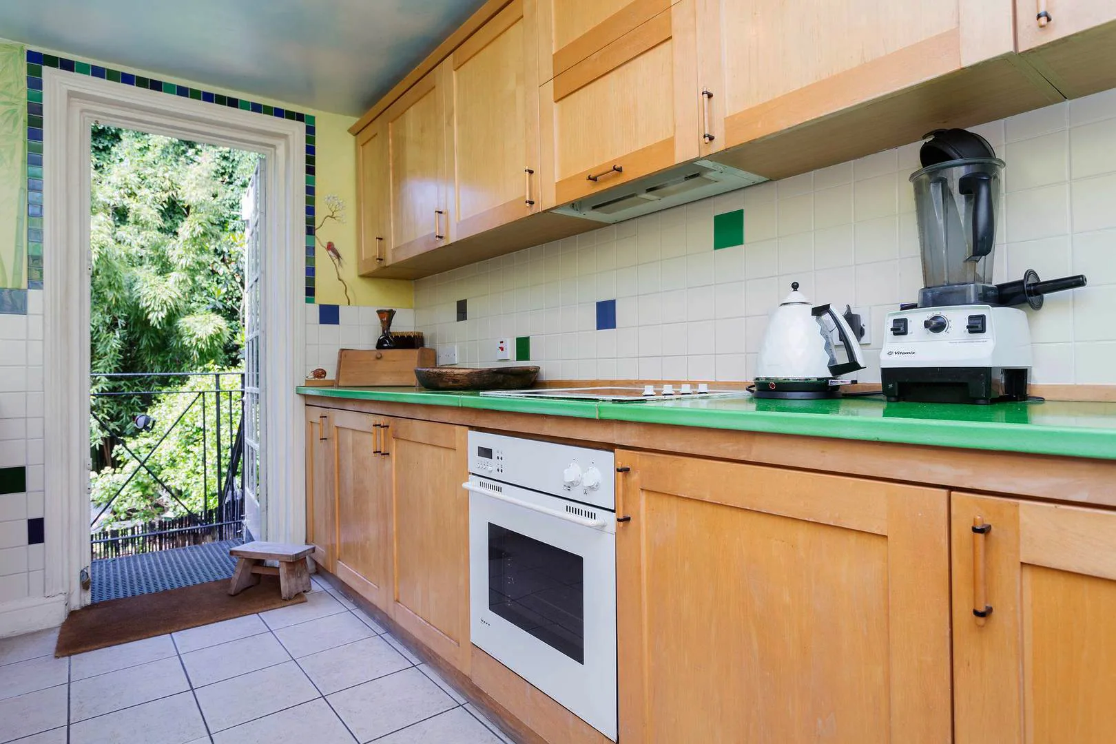A bright kitchen with wooden cabinets, a green countertop, and a glass door opening onto greenery.