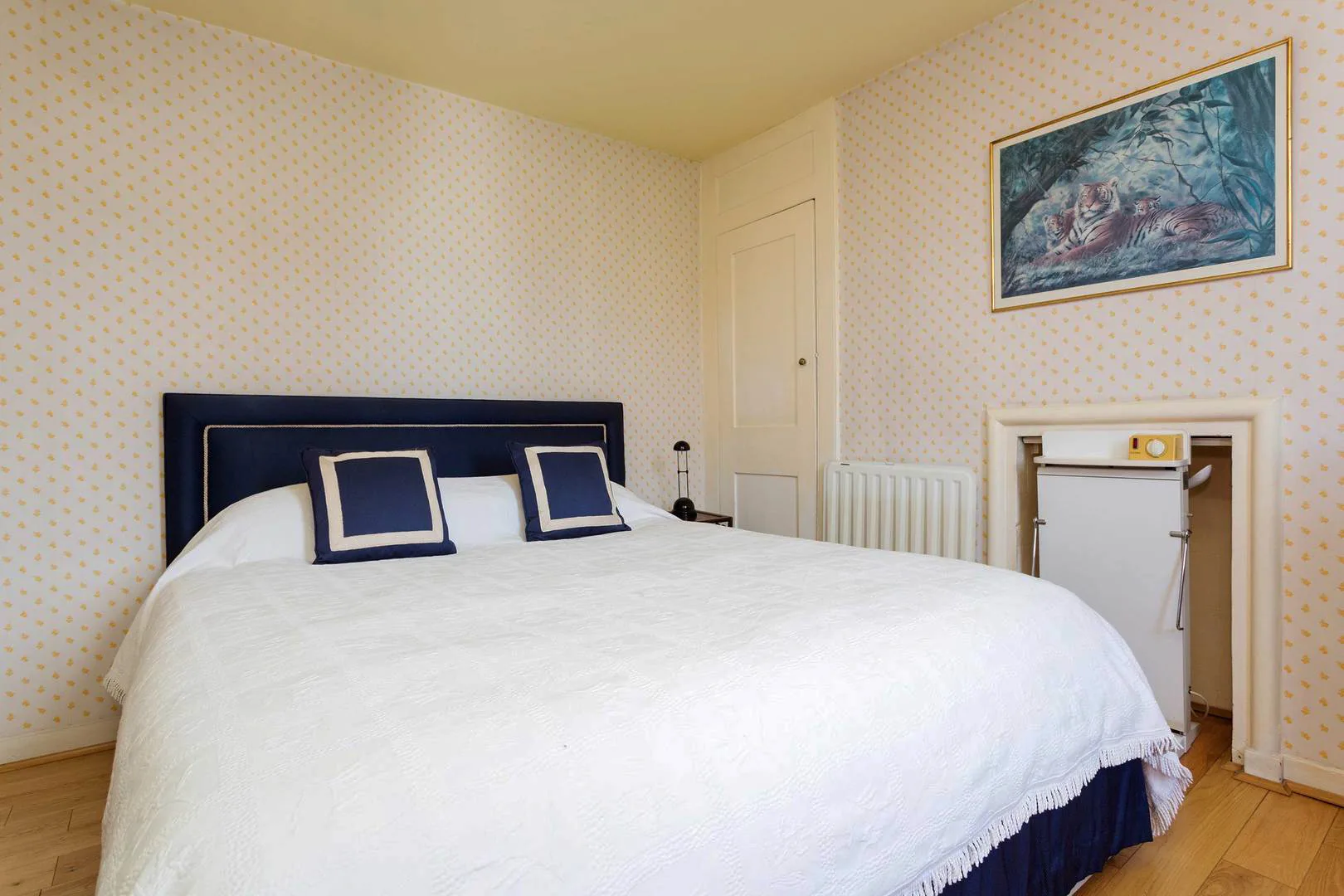 A bedroom with a large bed, patterned wallpaper, and framed artwork.