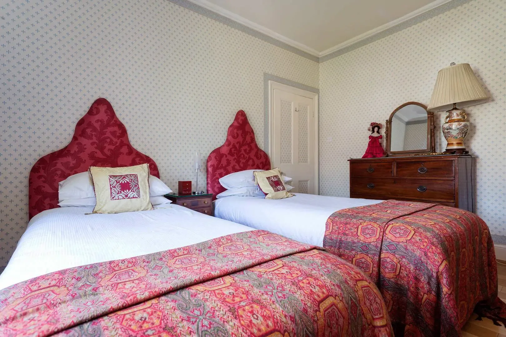 A bedroom with two beds, patterned bedding, and a wooden dresser.