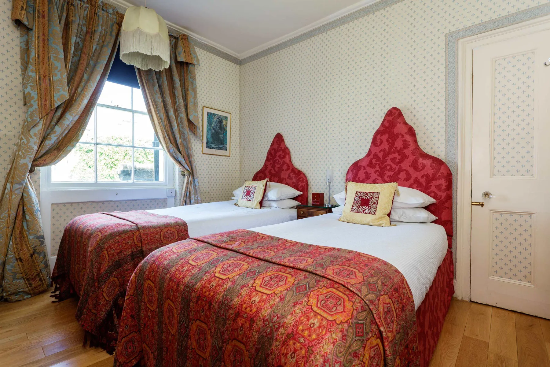 A bedroom with two beds dressed in patterned red and gold bedspreads.