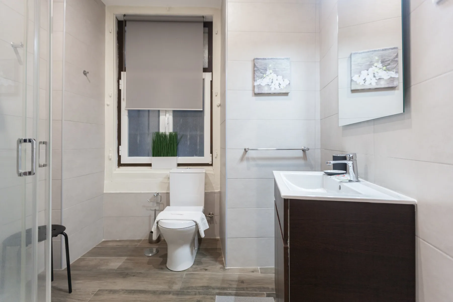 A tiled bathroom with a toilet, glass shower, and sink vanity.