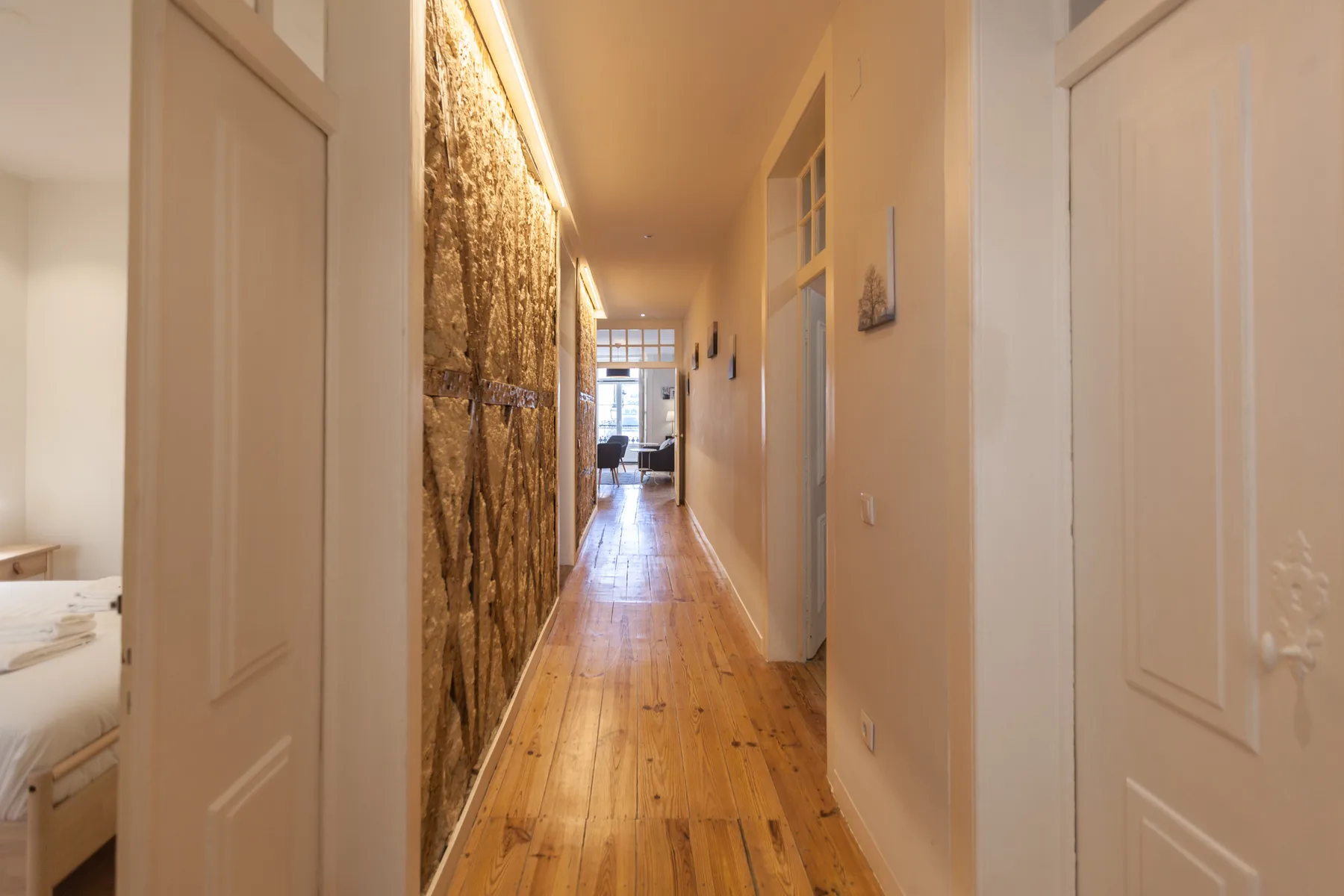A narrow hallway with wooden flooring leads toward a bright room.