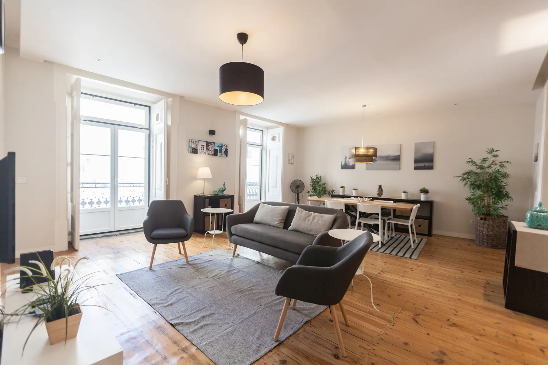 A bright living room with seating, a rug, and a dining area by tall windows.