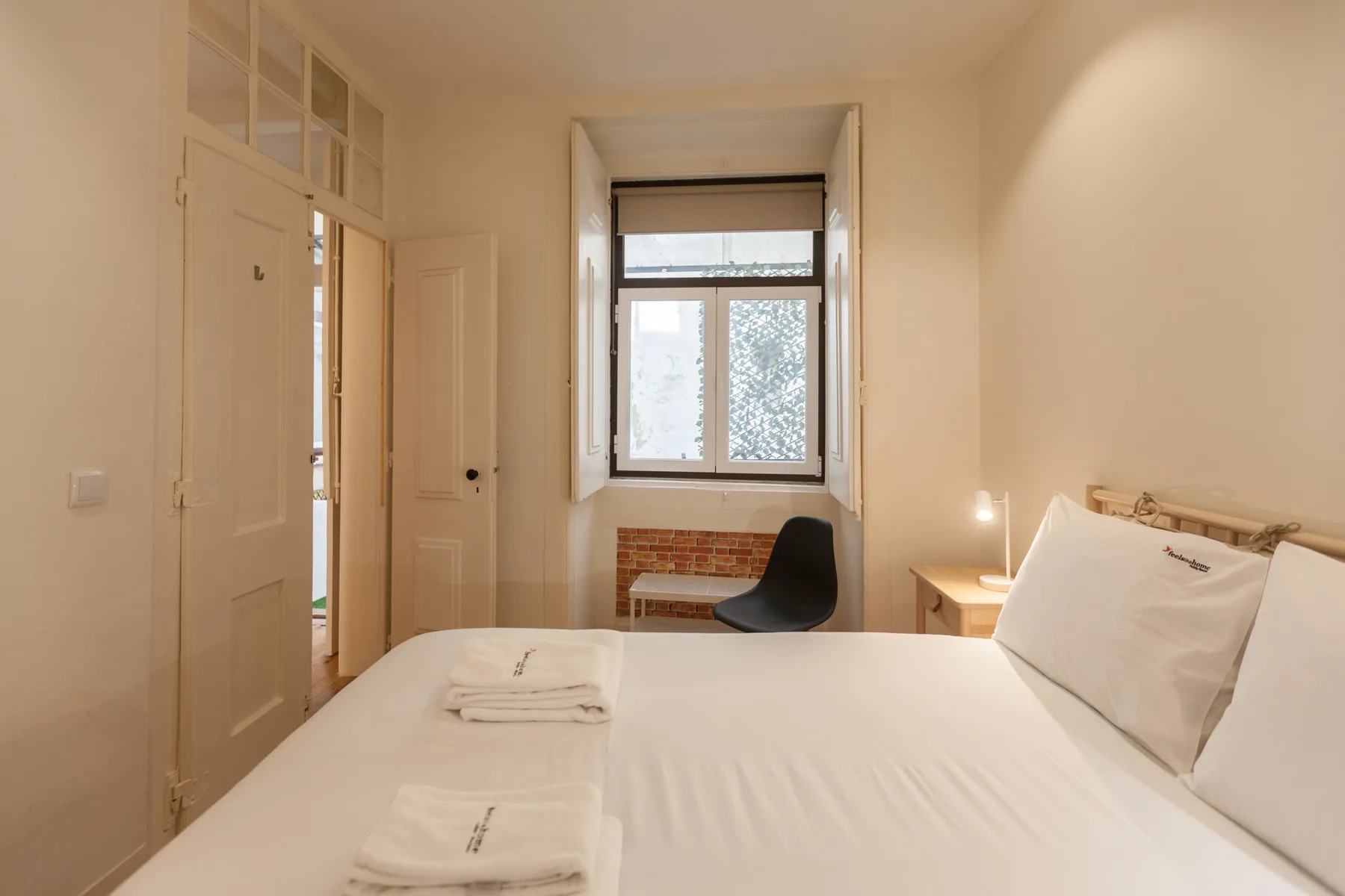 A bedroom with a neatly made bed and a window overlooking greenery.