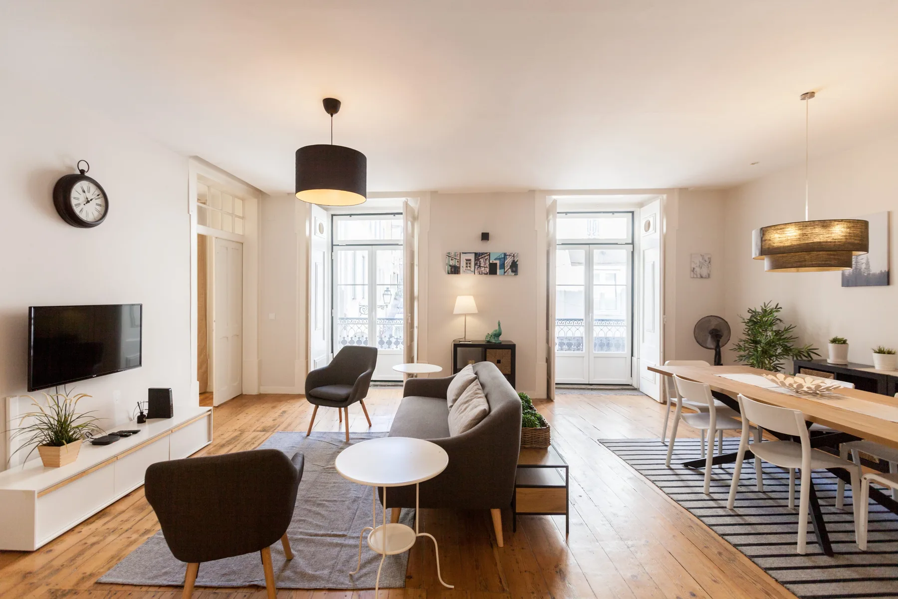 A bright living and dining room with seating, a television, and large windows.