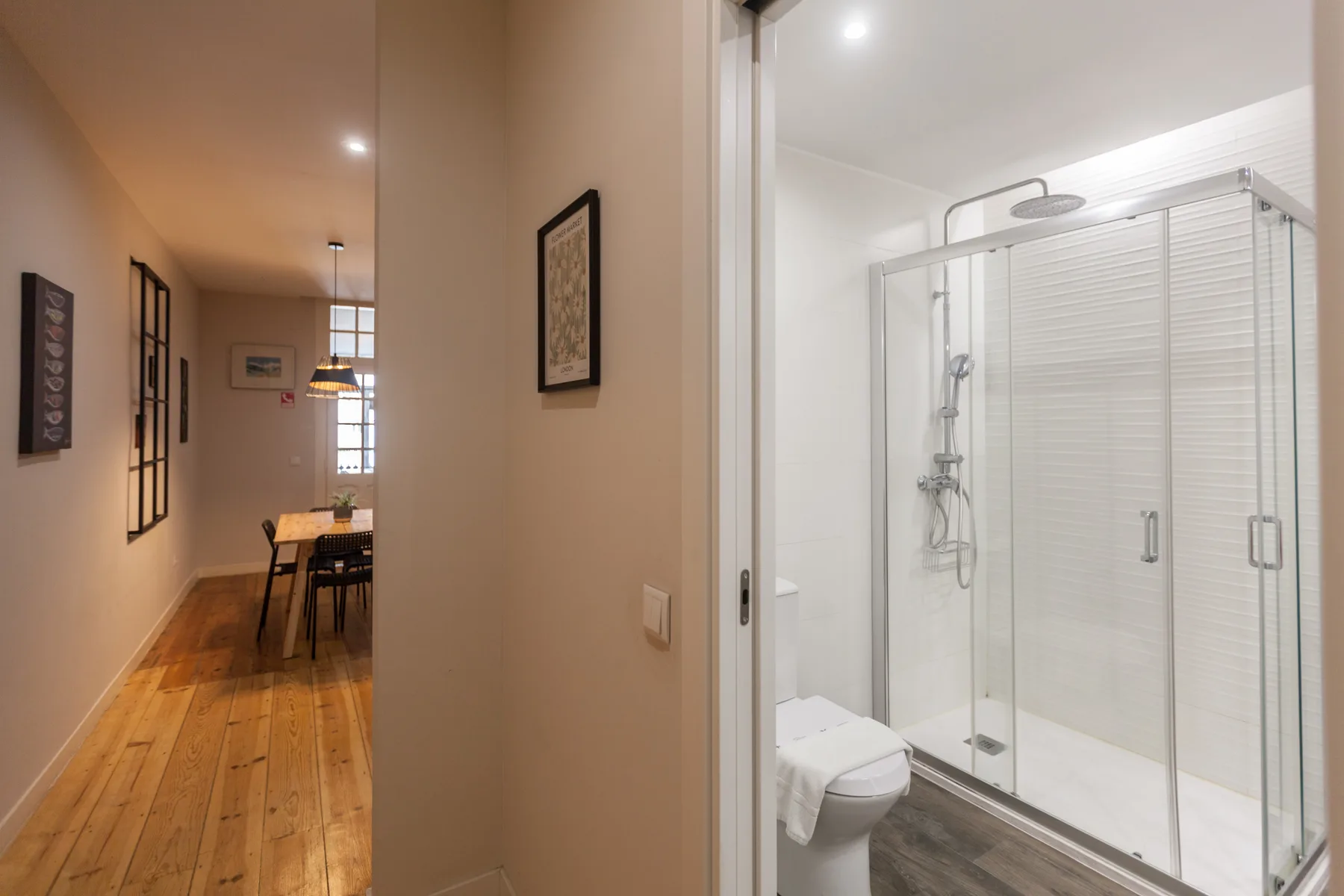 A hallway leads to a bathroom with a glass shower and toilet.