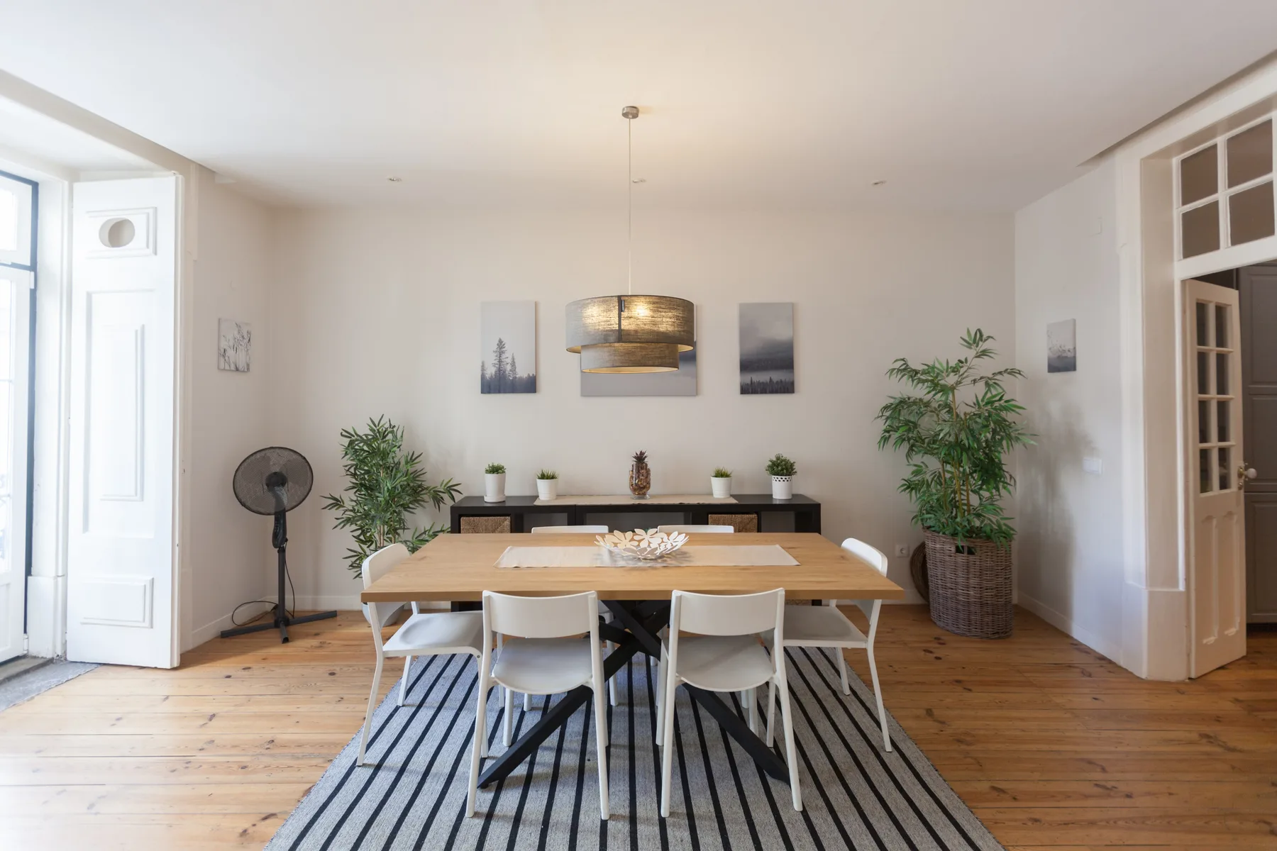 A dining area with a long wooden table, chairs, and plants.