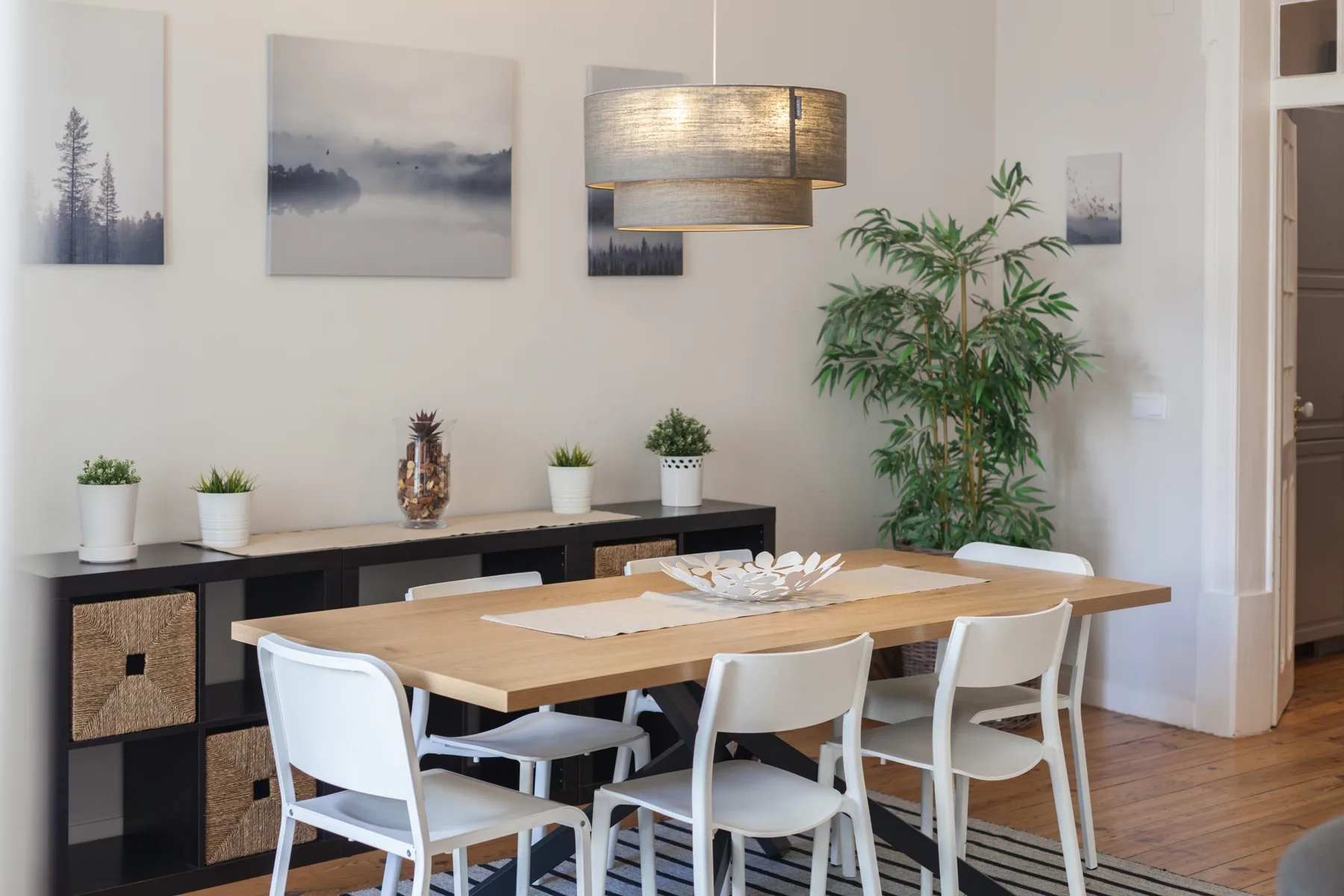A dining area with a wooden table, white seating, and potted plants.
